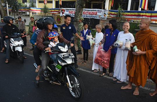 Motorcyclists passing the Dammadipa Arama Vihara on Jl. Raya Ma, Batu, Malang, East Java, get packages of sugary delicacies for breaking the fast, known locally as tajil, from Buddhist monks during the celebration of Vesak on Tuesday.